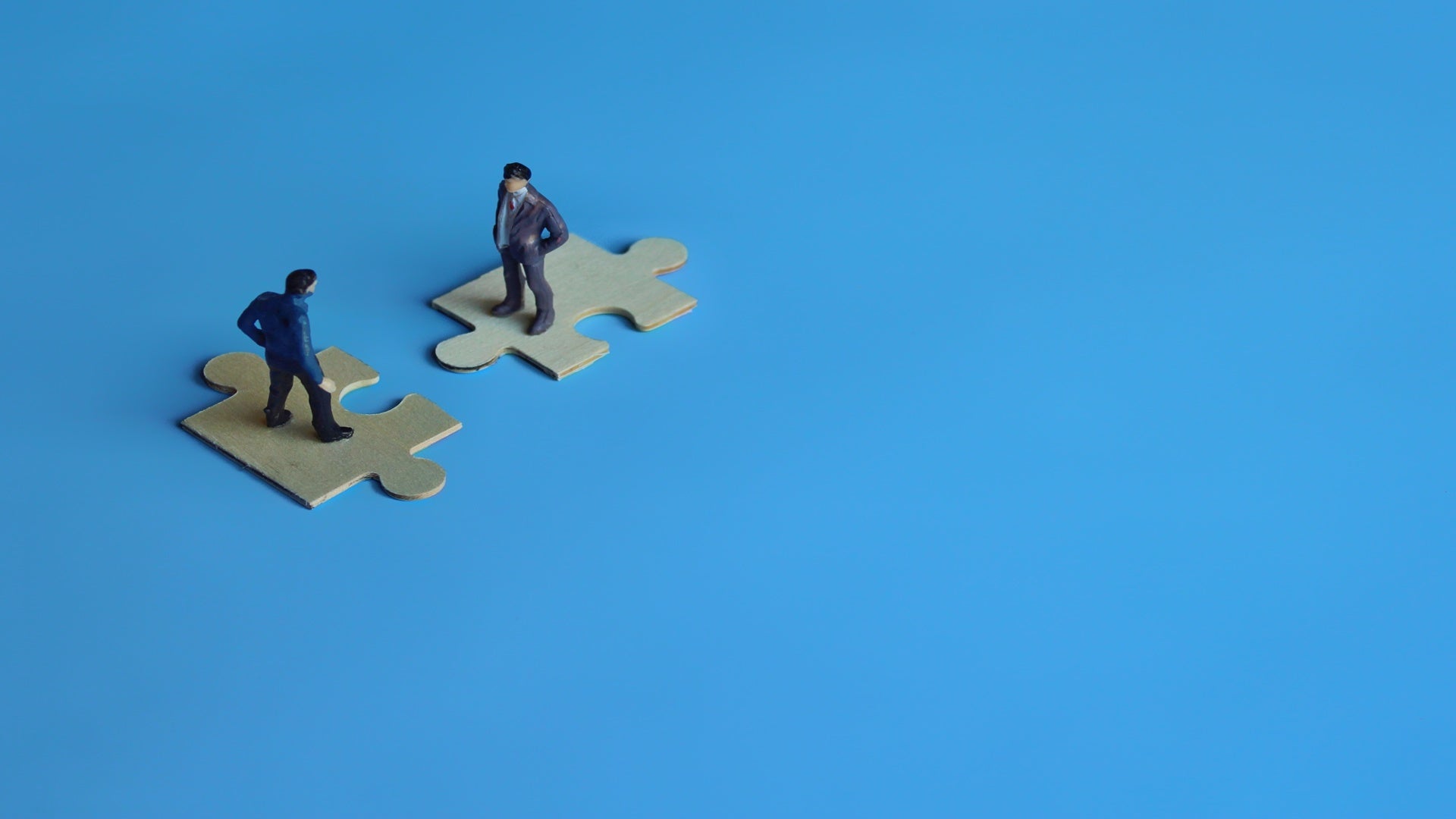 Business mergers and acquisitions, partnership concept. Two miniature people merging on puzzle. Copy space for text