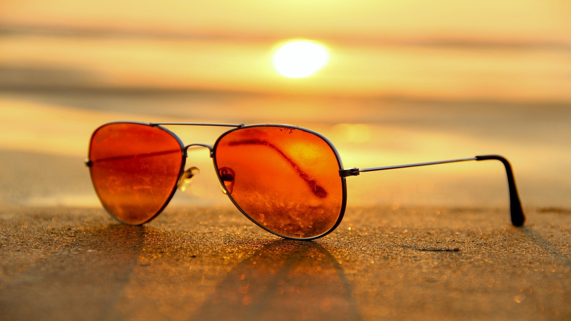Sunglasses, red lens, on a beach